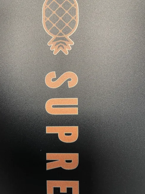 Screen printed heat transfer — copper rose gold pineapple logo applied to a dark surface